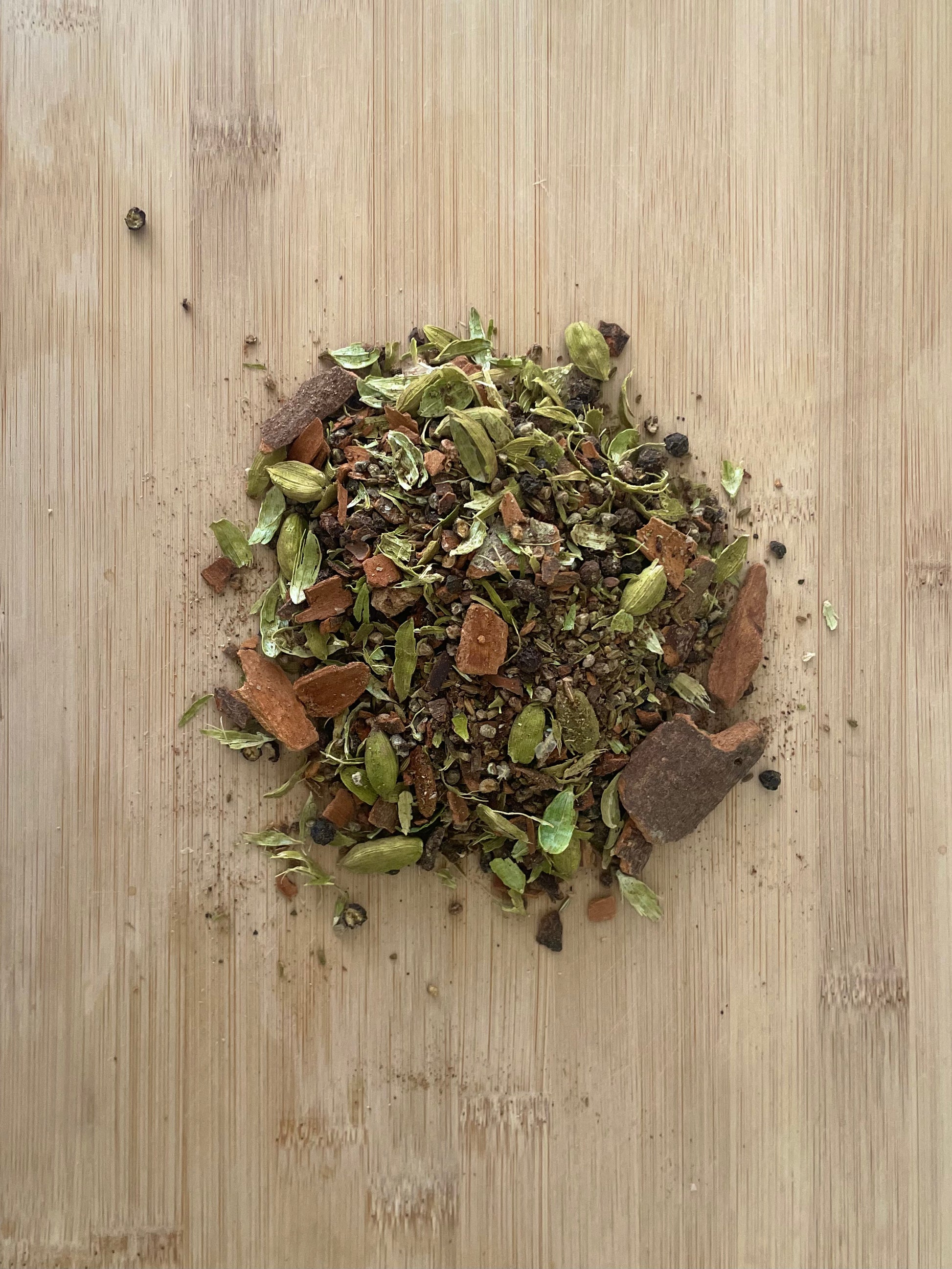 A mixture of spices (masalas) sitting on a wooden board, including cinnamon, cardamom, cloves, fennel, star anise, black pepper, and nutmeg