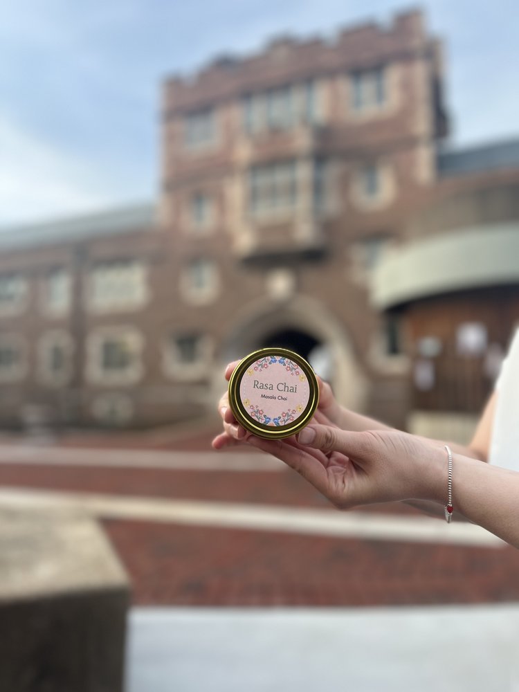 Hand holding a tin of Rasa Chai's masala chai in front of WashU's Brookings entrance